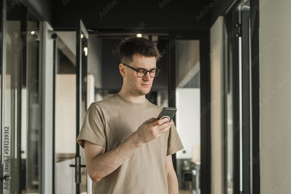 Young serious man using mobile phone in office building, internet, broadband, 5G. Portrait of pensive man in office Young serious man using mobile phone in office building, internet, broadband, 5G. Portrait of pensive man in office