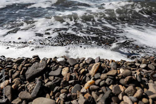 Tidal sea waves with foam on a gravel beach