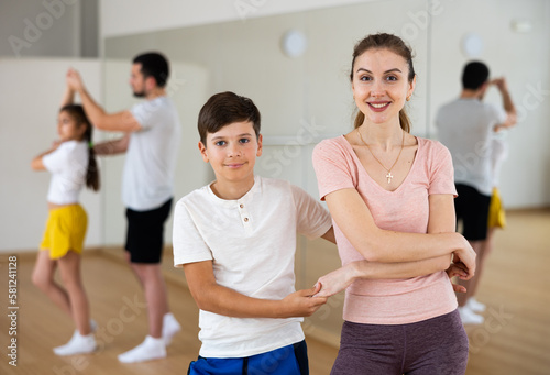 Cheerful young woman practicing active dance in pair with her tween son during family dance class. Children and parents bonding time