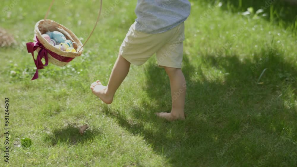 child's barefoot legs stepping green grass colorful Easter eggs in basket. traditional spring holiday celebration: little kid boy holding basket full of Easter eggs walking barefoot green lawn child's barefoot legs stepping green grass colorful Easter eggs in basket. traditional spring holiday celebration: little kid boy holding basket full of Easter eggs walking barefoot green lawn