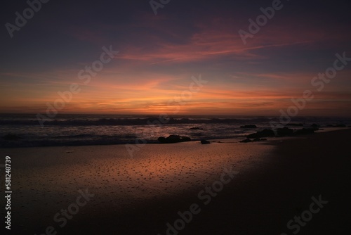 Last early spring daylight at Mangueta Beach  Zahora  Spain  faint reflections of the fading red orange sunset in the high above cirrus clouds still visible in the wet sand among dark beach boulders