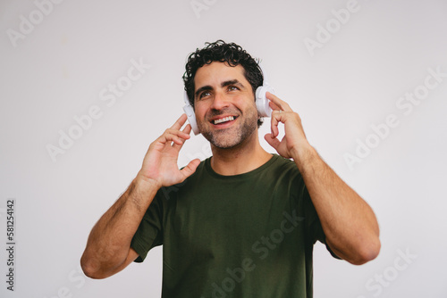 American shot of a middle-aged Latin man smiling while listening to music through his headphones on a white background.