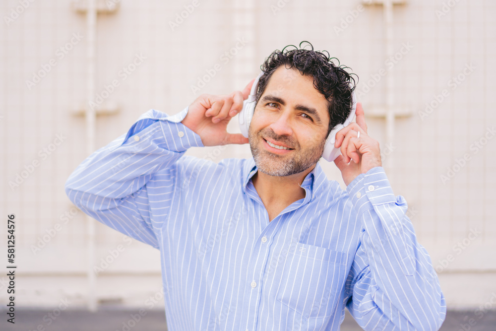 Middle-aged Latin man in oversized shirt looking at camera while wearing headphones. Middle-aged Latin man in oversized shirt looking at camera while wearing headphones.