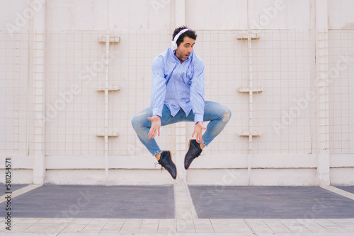 Casually dressed middle-aged Latin man wearing headphones while jumping trying to put his feet together.