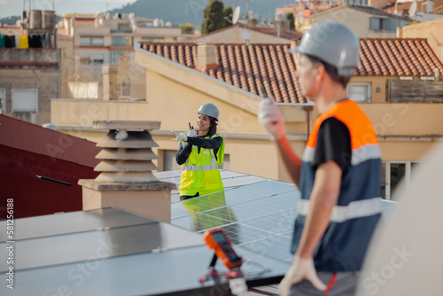 Technical engineer woman pointing away, using walkie talkie or Portable radio transceiver during solar panel system installation on the roof of a building. Horizontal and focused background