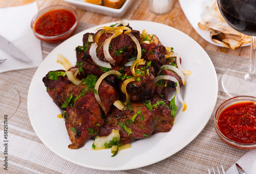 Oriental grilled pork meat shashlik with sliced onion rings on a white ceramic plate