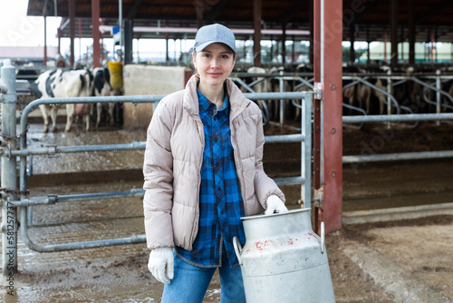 Milkmaid standing with aluminium cans near open cowshed at dairy farm