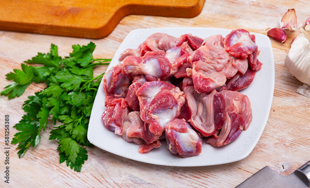 Fresh chicken gizzards on plate on wooden background with parsley, garlic and onion