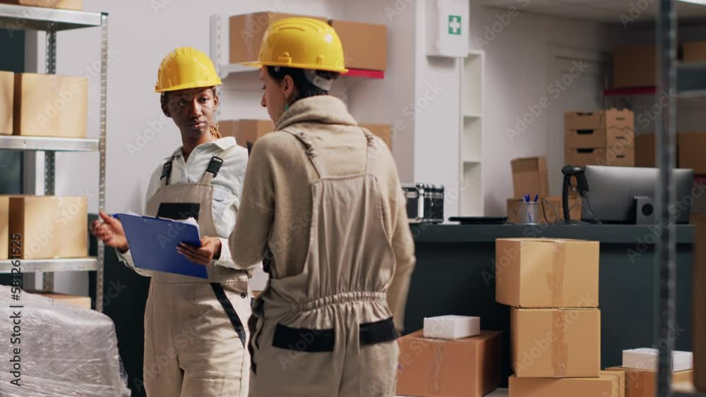 Team of women talking about package delivery service in storage room, examining stock in cardboard boxes. Diverse people checking merchandise and products in warehouse. Tripod shot. Team of women talking about package delivery service in storage room, examining stock in cardboard boxes. Diverse people checking merchandise and products in warehouse. Tripod shot.