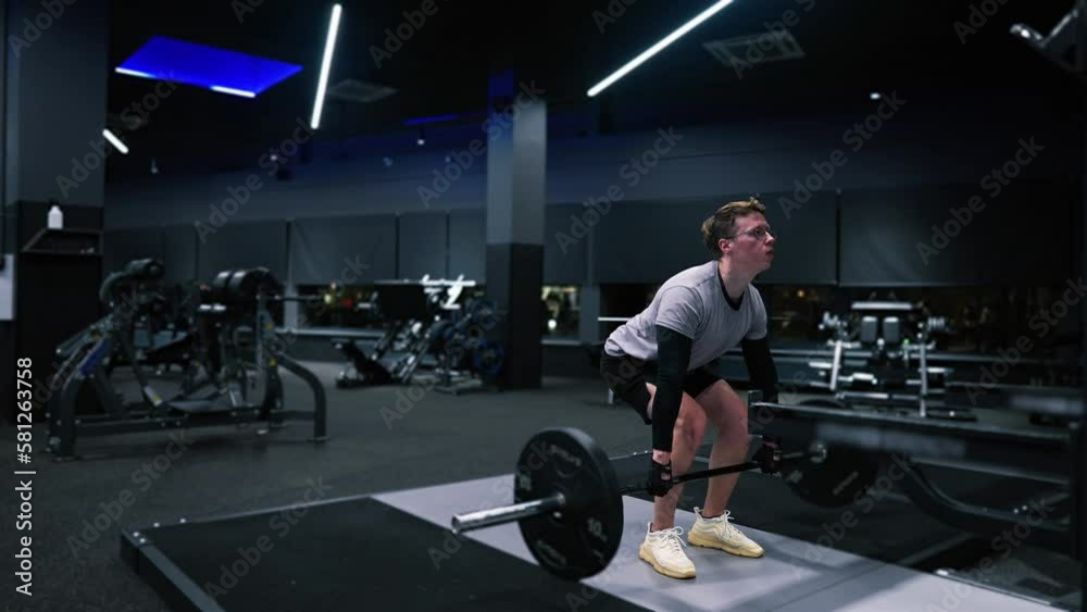 Fitness man trains in a modern gym and does an exercise with a barbell, weightlifting, deadlift, squats with a barbell, lifting the barbell slow motion Fitness man trains in a modern gym and does an exercise with a barbell, weightlifting, deadlift, squats with a barbell, lifting the barbell slow motion