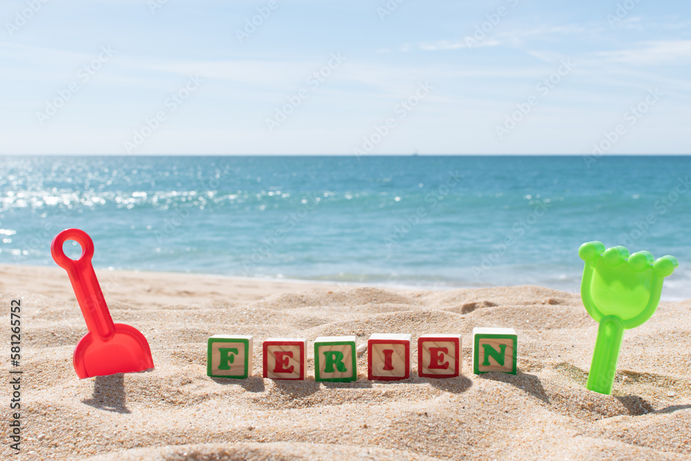Ferien (German Holiday) letters on cubes in the sand and ocean in the background. Copy space. Vacations background. Kids sand toys. Ferien (German Holiday) letters on cubes in the sand and ocean in the background. Copy space. Vacations background. Kids sand toys.