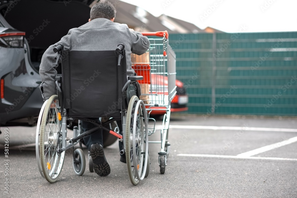 a disabled person on a wheelchair pushes a shopping trolley in front of him