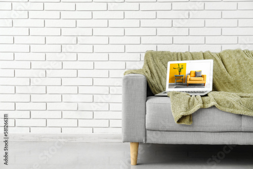 Sofa and laptop with open page of online furniture store near white brick wall. Banner for design