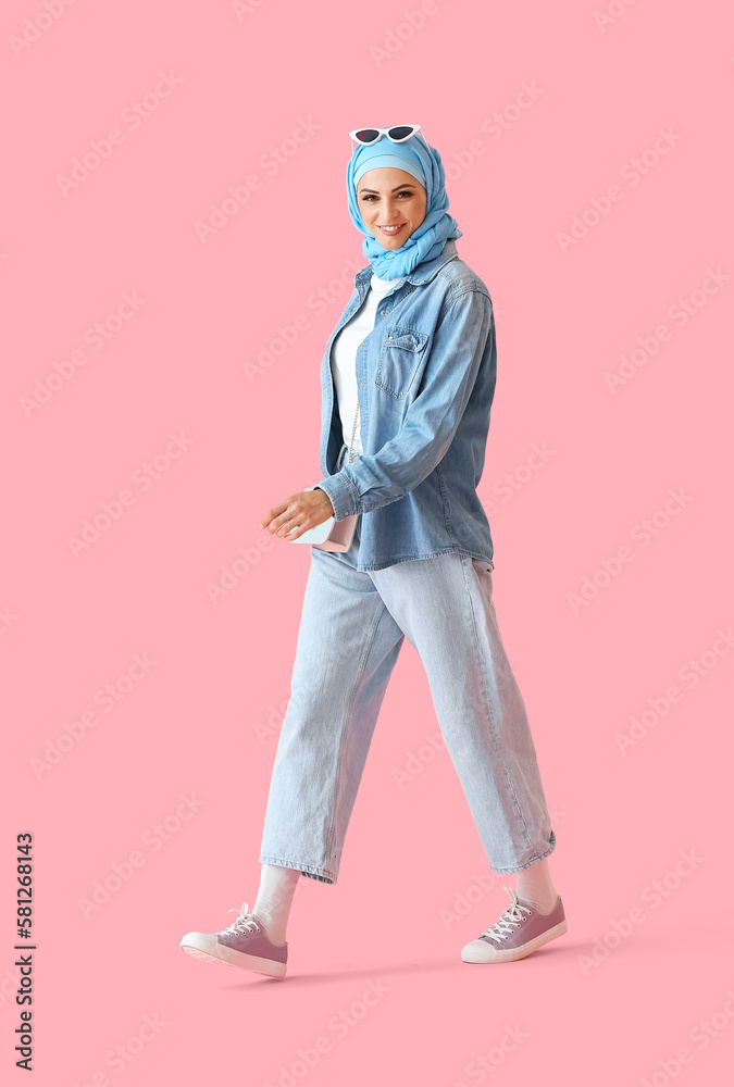 Stylish Muslim woman in blue hijab walking on pink background Stylish Muslim woman in blue hijab walking on pink background