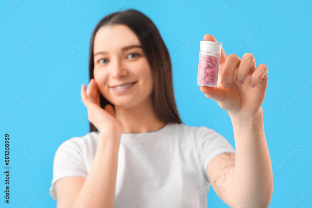 Young woman with bottle of vitamin supplements on blue background, closeup Young woman with bottle of vitamin supplements on blue background, closeup