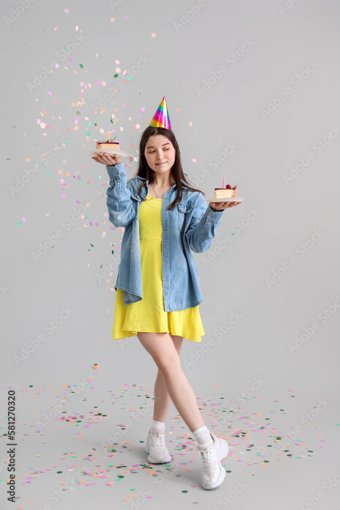 Thoughtful young woman with Birthday cakes on grey background