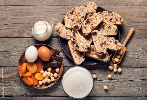 Fotografi Delicious biscotti cookies, dried apricots, hazelnuts, chocolate and milk on woo