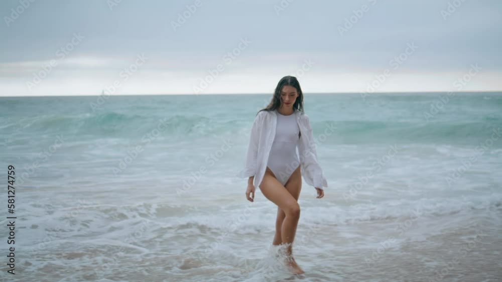 Woman walking sea foam in sexy white swimsuit. Young girl going on ocean beach. Woman walking sea foam in sexy white swimsuit. Young girl going on ocean beach.