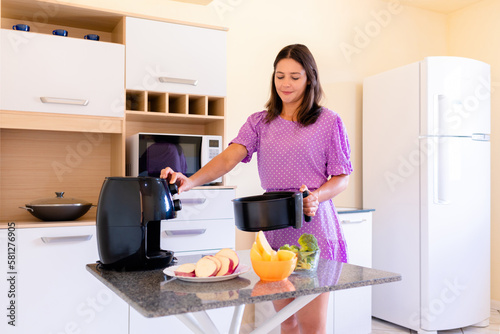 Brazilian woman using air fryer to fry food in home kitchen. Electric fryer without oil.