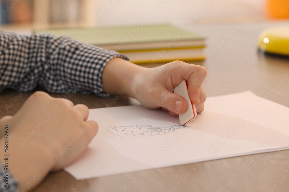 Boy erasing mistake in his notebook at wooden desk indoors, closeup Boy erasing mistake in his notebook at wooden desk indoors, closeup