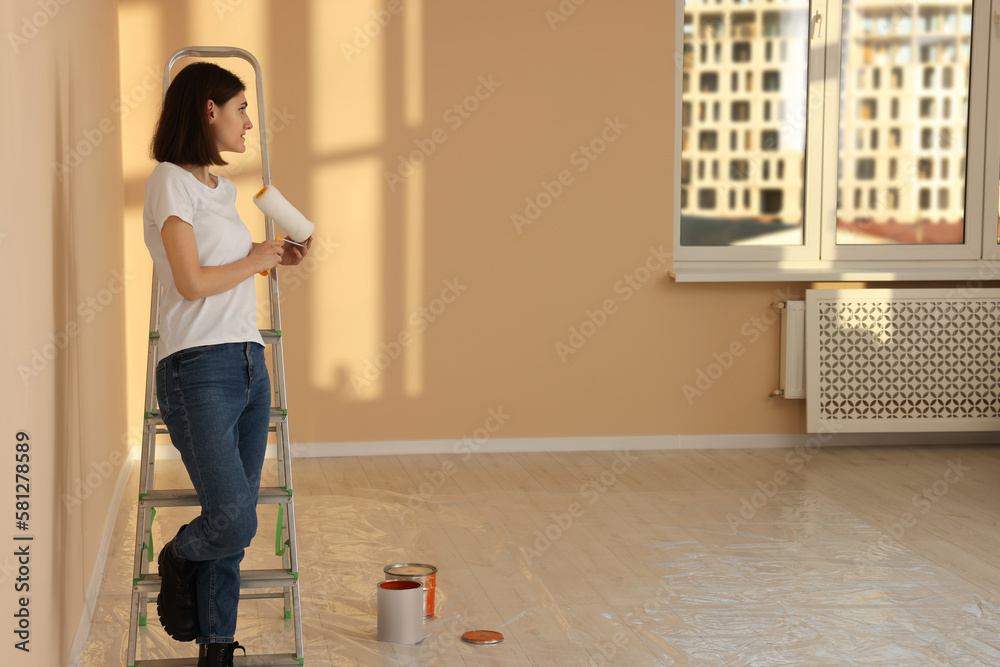 Young woman with roller near metal stepladder indoors. Room renovation Young woman with roller near metal stepladder indoors. Room renovation