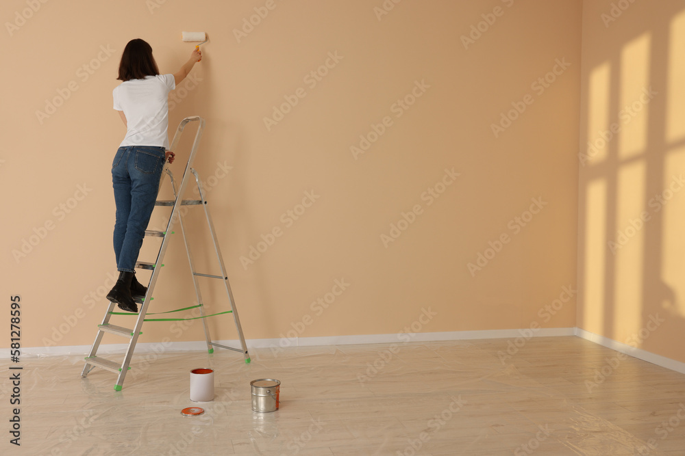 Young woman painting wall with roller on stepladder indoors, space for text. Room renovation Young woman painting wall with roller on stepladder indoors, space for text. Room renovation