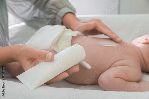 Mother applying moisturizing cream onto baby s back on changing table  closeup