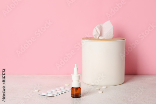 Nasal drops with pills and tissue box on table near pink wall. Allergy concept