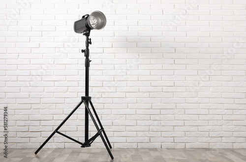 Foto Professional studio flash light with reflector on tripod against white brick wall indoors, space for text