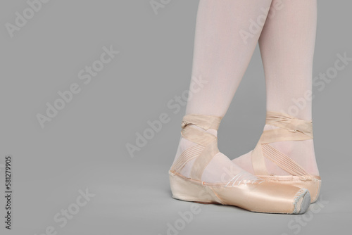 Young ballerina in pointe shoes practicing dance moves on grey background, closeup. Space for text