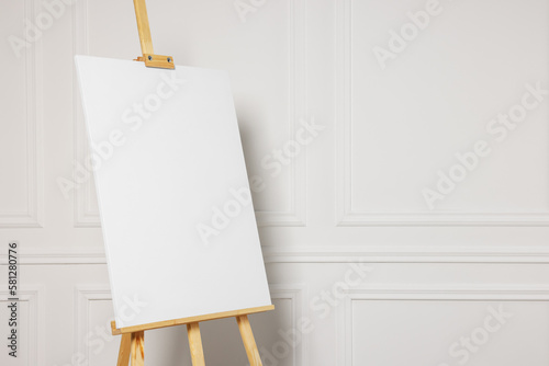 Photo Wooden easel with blank canvas near white wall. Space for text