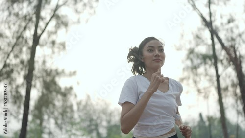 Slow-Motion of young sport Asian woman running on the road in nature outdoor, happy and freshness lifestyle for healthy workout exercise, jogger or runner girl training in the morning