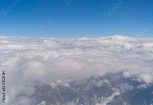 Airplane jet flying above clouds view with blue sky from the window in traveling and transportation concept. Nature landscape background. © tampatra