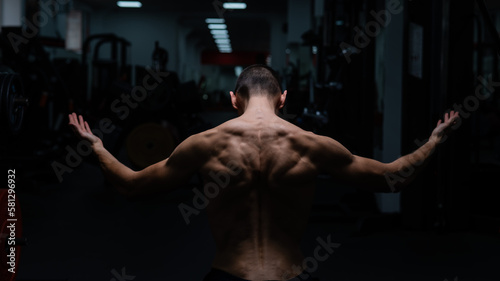 Back view of shirtless man with sculpted body in gym. 
