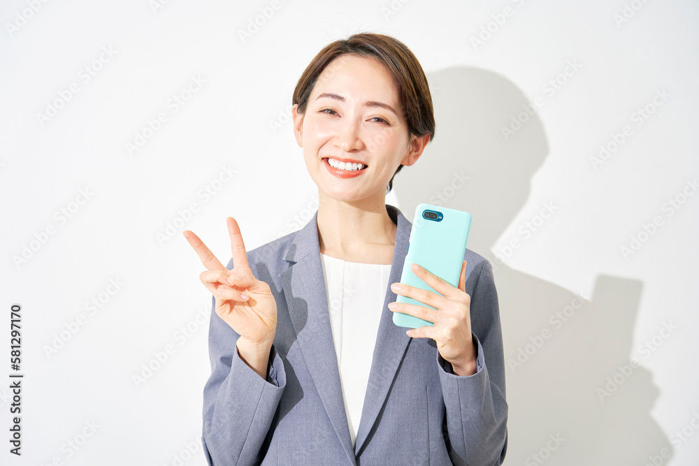 スマートフォンを持ってピースサインをするビジネスウーマン 白背景 スマートフォンを持ってピースサインをするビジネスウーマン 白背景