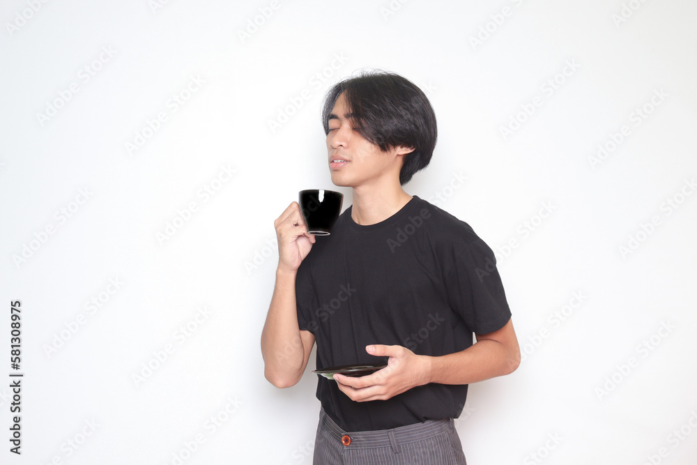 Portrait of handsome Asian man in black t-shirt drinking a cup of coffee while holding the saucer. Isolated image on white background Portrait of handsome Asian man in black t-shirt drinking a cup of coffee while holding the saucer. Isolated image on white background