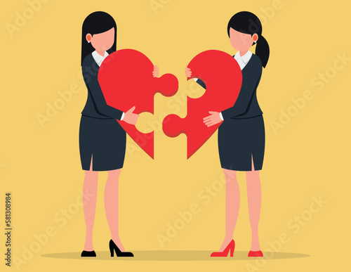 Business metaphor of a joint venture, partnership or teamwork. Two Business women joining together heart shaped jigsaw puzzle.