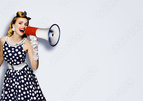 Portrait image of beautiful woman holding mega phone, shout, saying, advertising. Pretty girl in black pin up style dress with megaphone loudspeaker. Isolated light gray grey background. Big sales ad.