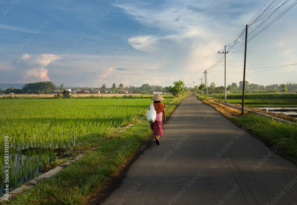 A woman going to work at the farm in the morning with beautiful landscape as background.