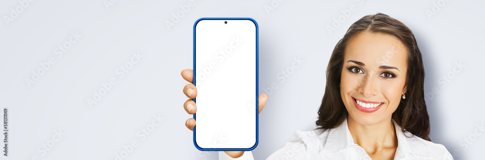 Image of excited smiling young woman in confident cloth, holding show smartphone cell phone mobile with white blank mock up screen, isolated grey gray background. App application ad Image of excited smiling young woman in confident cloth, holding show smartphone cell phone mobile with white blank mock up screen, isolated grey gray background. App application ad