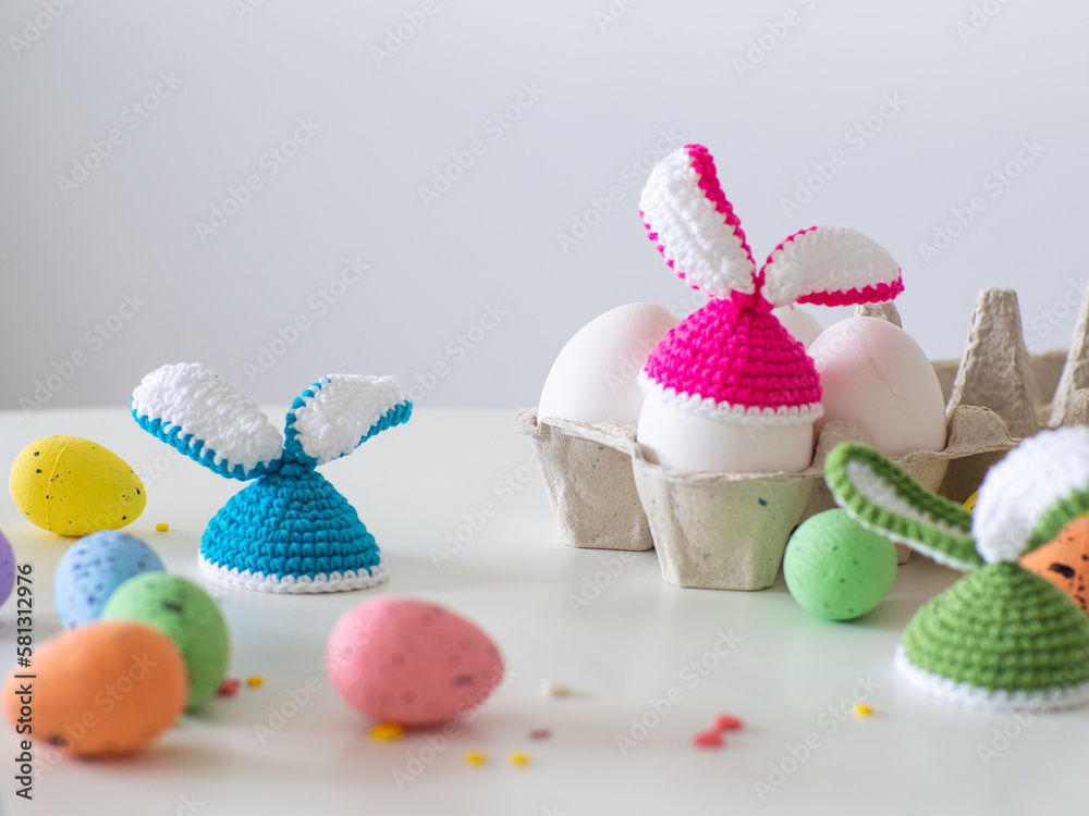 Colotful crochet hats with ears for Easter eggs. Crocheted hat with bunny ears. Easter Greeting card. Happy Easter holiday concept with cute handmade eggs with knitted bunny hats with copy space.
