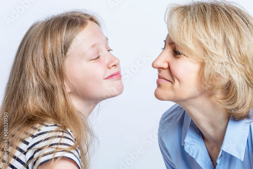 Mom and daughter smile and look at each other. Love and tenderness in family relationships. Light background. Close-up.