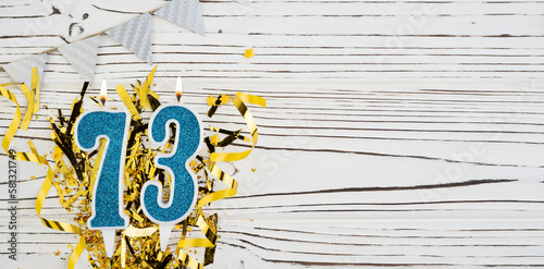 Number 73 blue celebration candle on white wooden background with golden foil. Copy space.