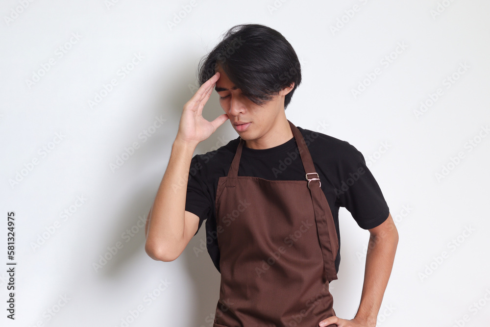 Portrait of attractive Asian barista man in brown apron holding hand on forehead, forgets something, and regrets himself. Isolated image on white background Portrait of attractive Asian barista man in brown apron holding hand on forehead, forgets something, and regrets himself. Isolated image on white background