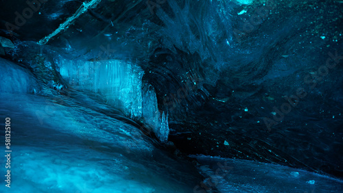 Turquoise pure color of ice inside the ice cave. Stones and icicles are visible in places. Light grains of snow on the ice walls. Frozen air bubbles in an ice wall. An ancient glacier. Color gradient