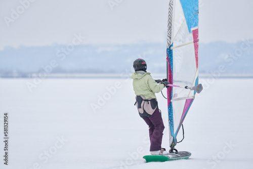 A middle-aged woman, a snowsurfer, rides a sailboard. Snowsurfing on a cloudy winter day. photo