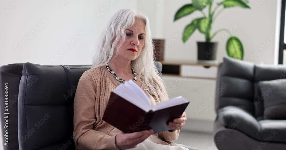 Elderly woman with gray hair reading book at home on couch 4k movie slow motion Elderly woman with gray hair reading book at home on couch 4k movie slow motion