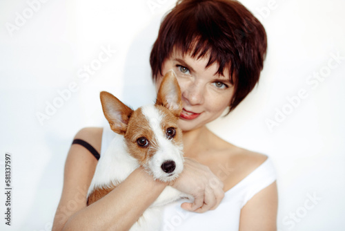 Portrait of good looking cheerful woman enjoys company of small pedigree dog wears white tank top spends free time with favorite pet isolated over white background. Animal owner