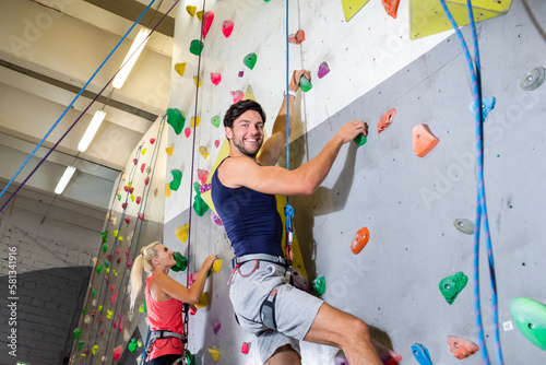 Couple of Caucasian Athletes Climbing Up Together on Steep Rock climbing on artificial wall indoors As Extreme sports and bouldering concept.