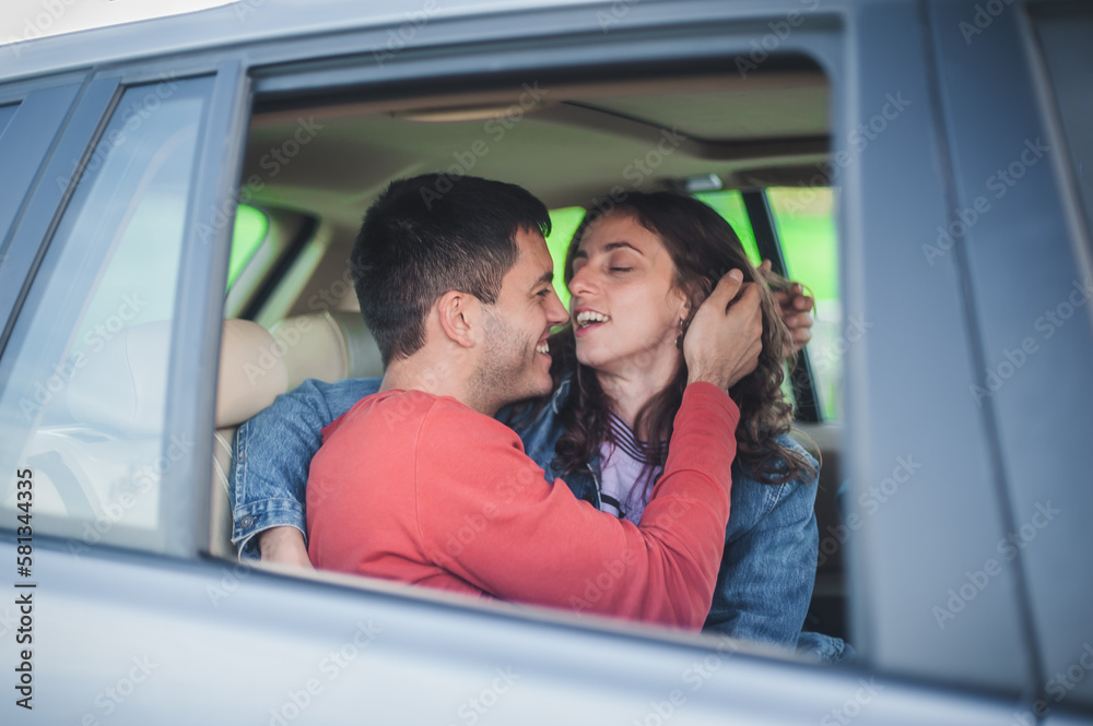 View through the window. Young smiling and cheerful couple in love, sitting in the back seat, looking and kissing passionately each other. Happiness and love concept